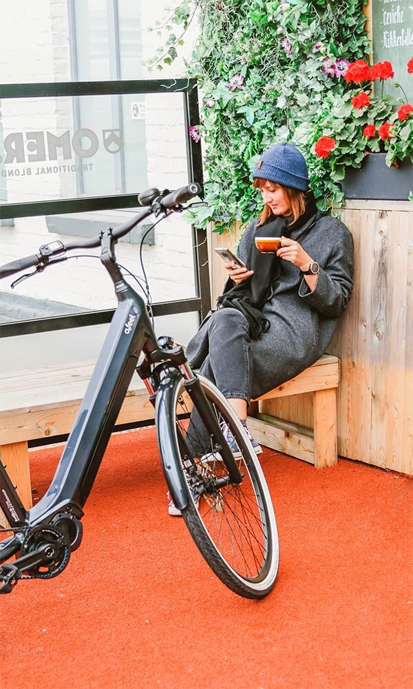 A woman drinking coffee on a terrace with her ebike near by