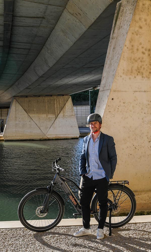 A smart dressed man in front of an electric bike, under a bridge